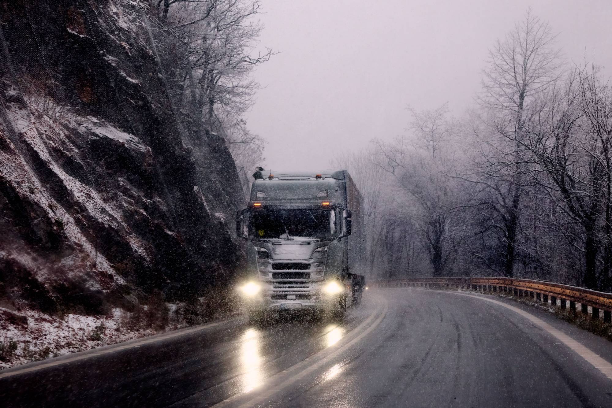 Heavy-duty truck driving through snow on a winding mountain road
